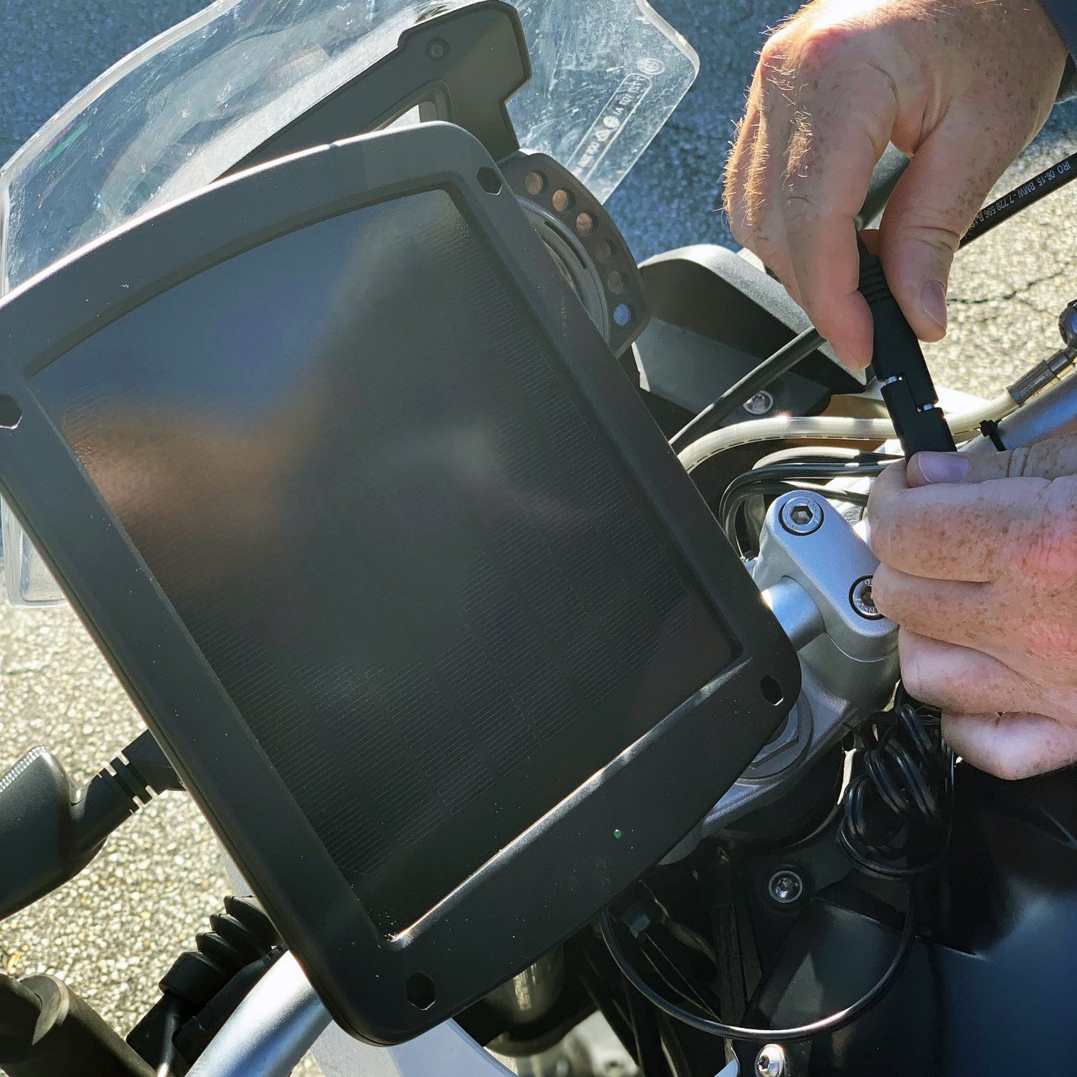 Person adjusting a motorcycle mount with a solar panel on a bike