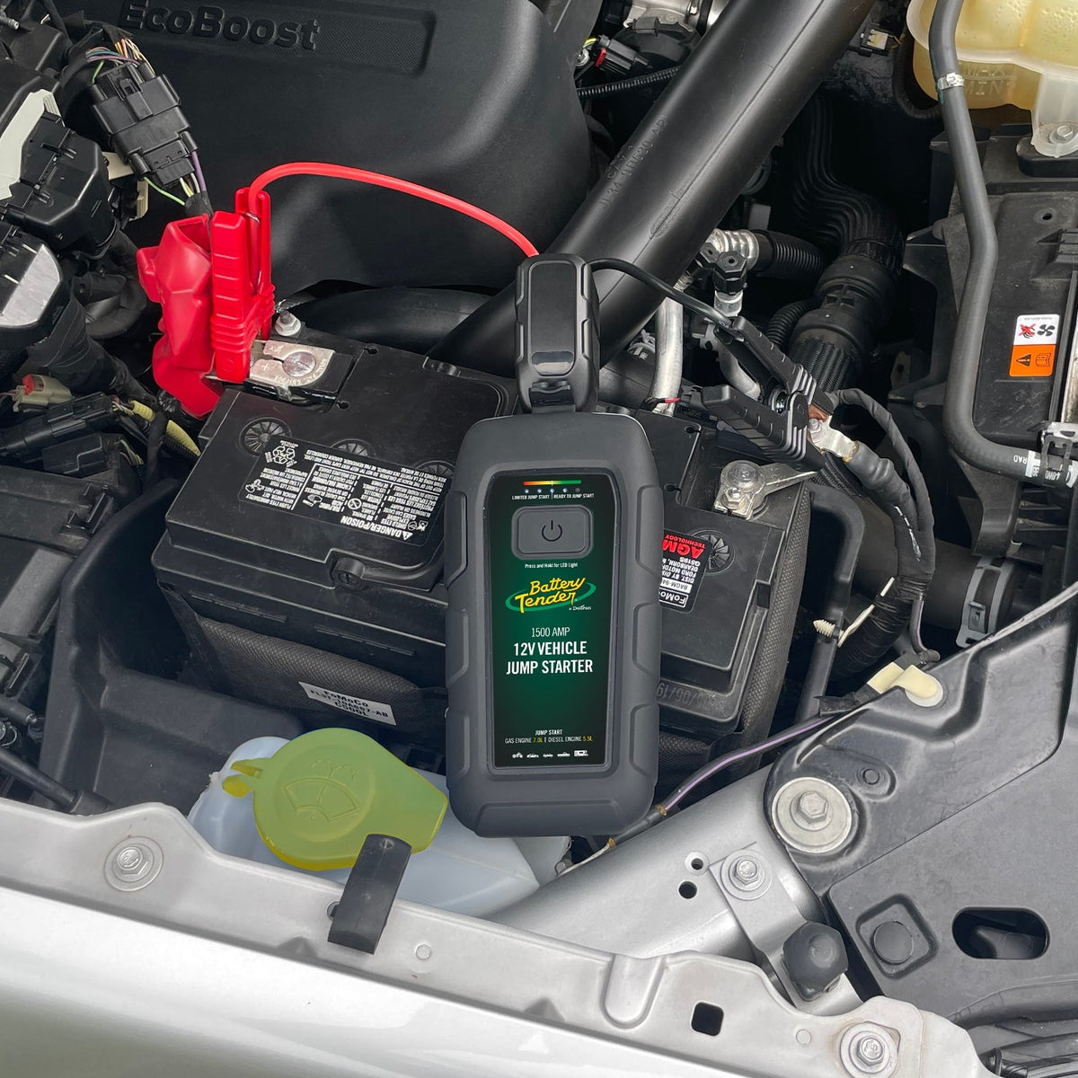 Person using a Battery Tender® portable jump starter to jumpstart a battery on a car in a parking lot